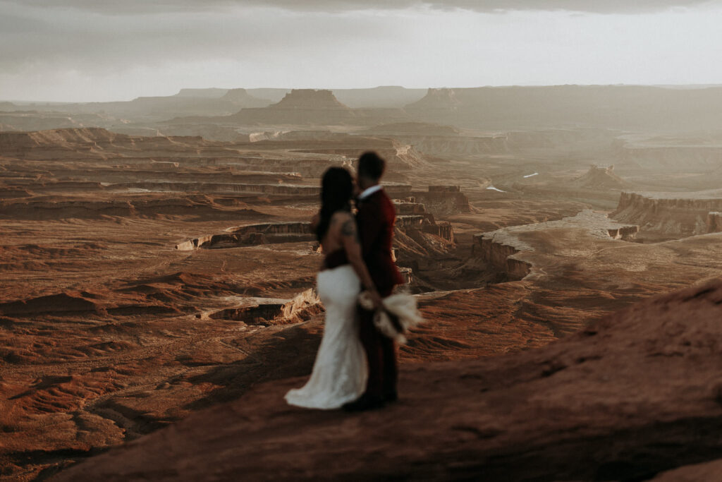 A boho elopement couple looking out at a panoramic landscape at Canyonlands National Park in Moab, Utah. 