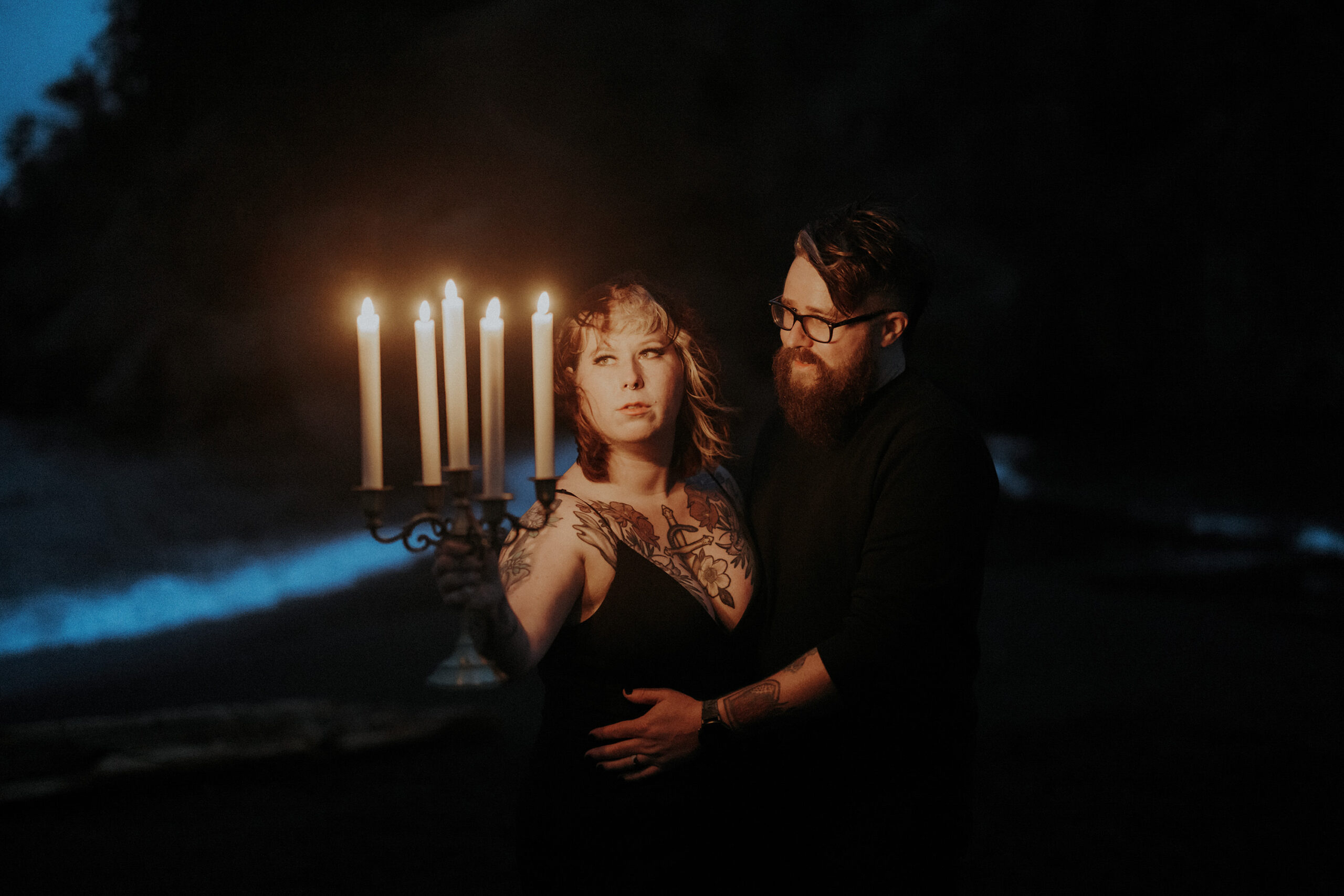 A couple dressed in black at night on a black beach with a candelabra.