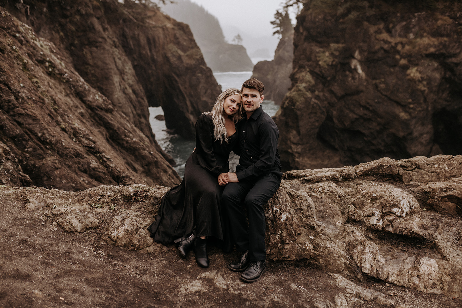 A wedding couple dressed in all black on the southern Oregon coast surrounded a rock formations and the ocean.