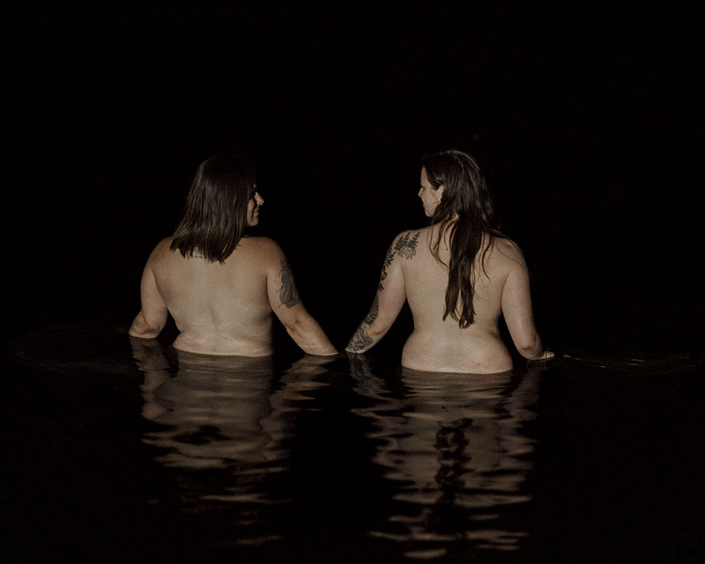 Two nude women in a lake at night walking away