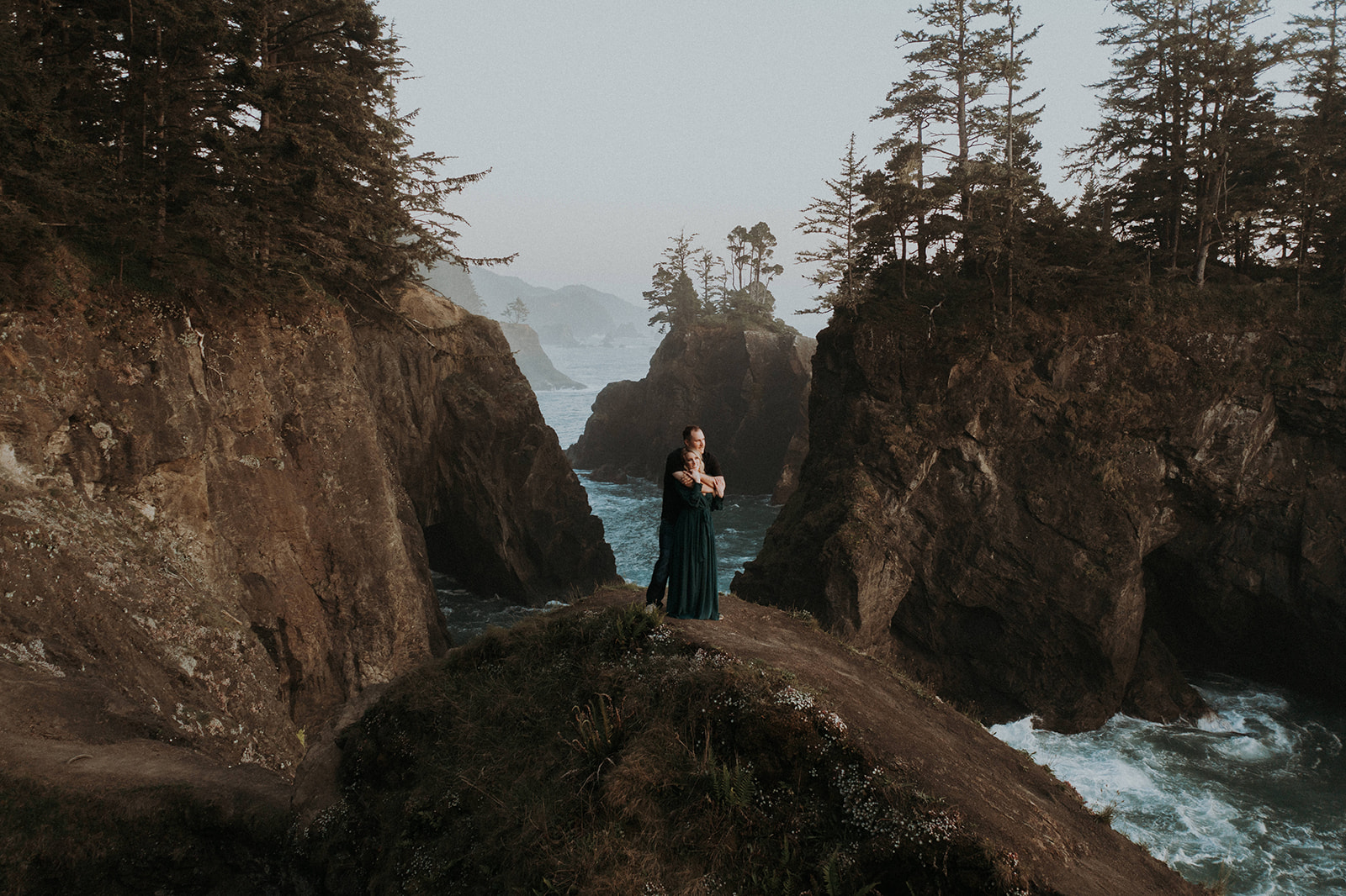 An engaged couple standing on a rock arch at Natural Bridges in Oregon at sunset.