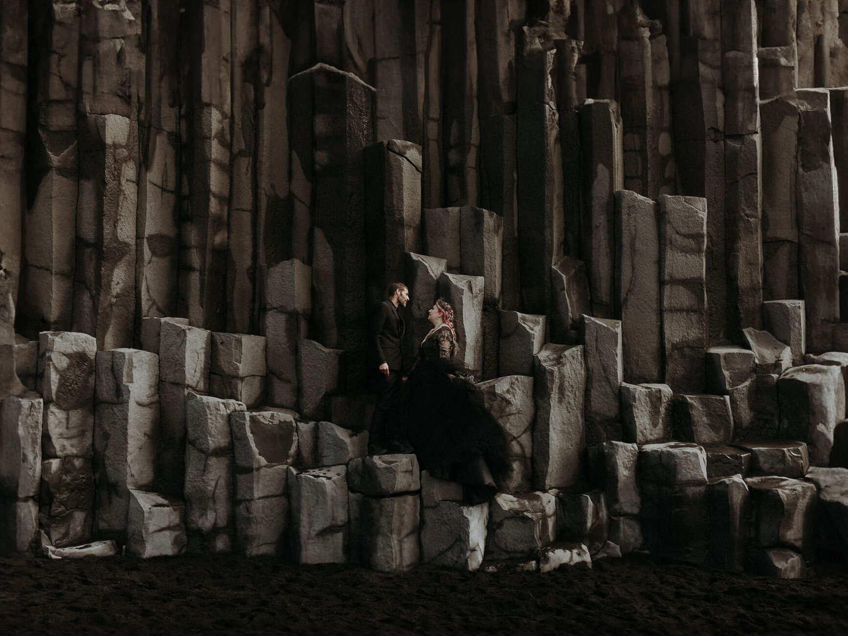 A wedding couple dressed in black standing on basalt pillars at Reynisfjara black beach in Iceland.